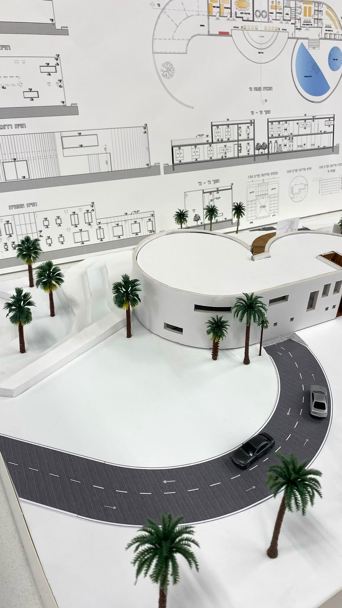 Physical model of the clinic project seen from above, with working drawings in the background