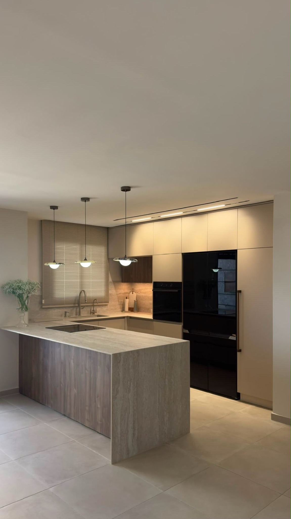 The Orian kitchen after installation: travertine island facing the dark appliance wall