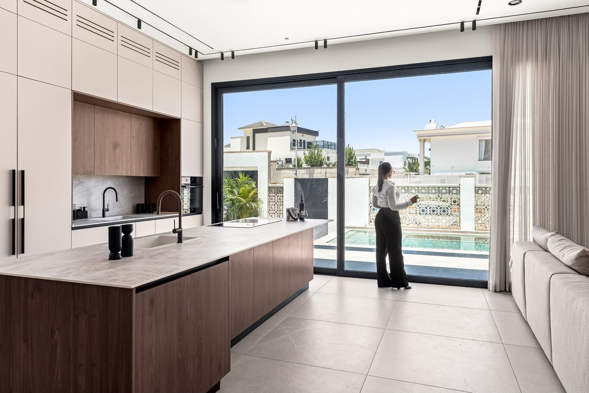 Keily at the pale stone island of the mist-grey and walnut kitchen, black taps to either side