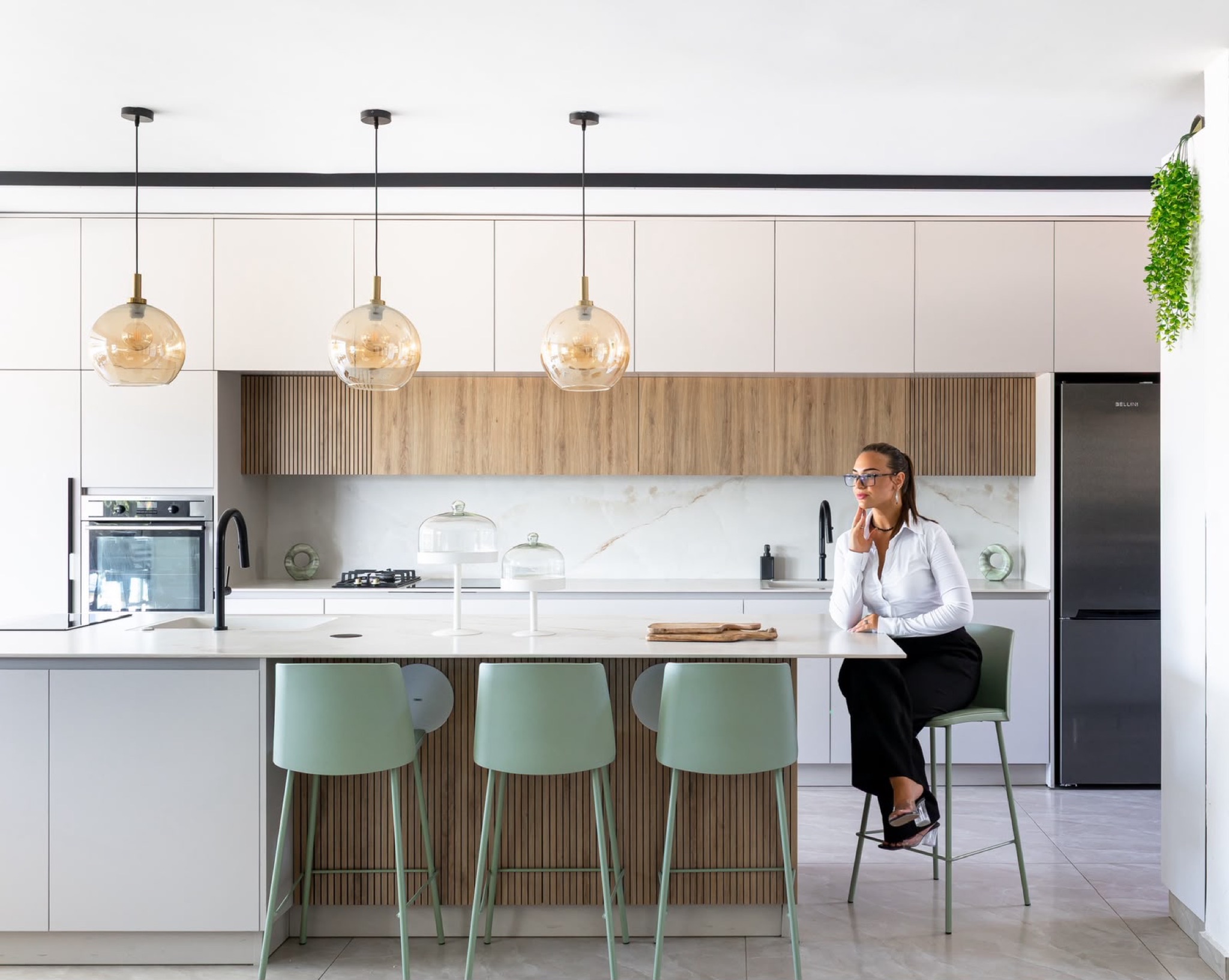 The oak-slat kitchen under amber glass pendants, sage green stools drawn up to the island